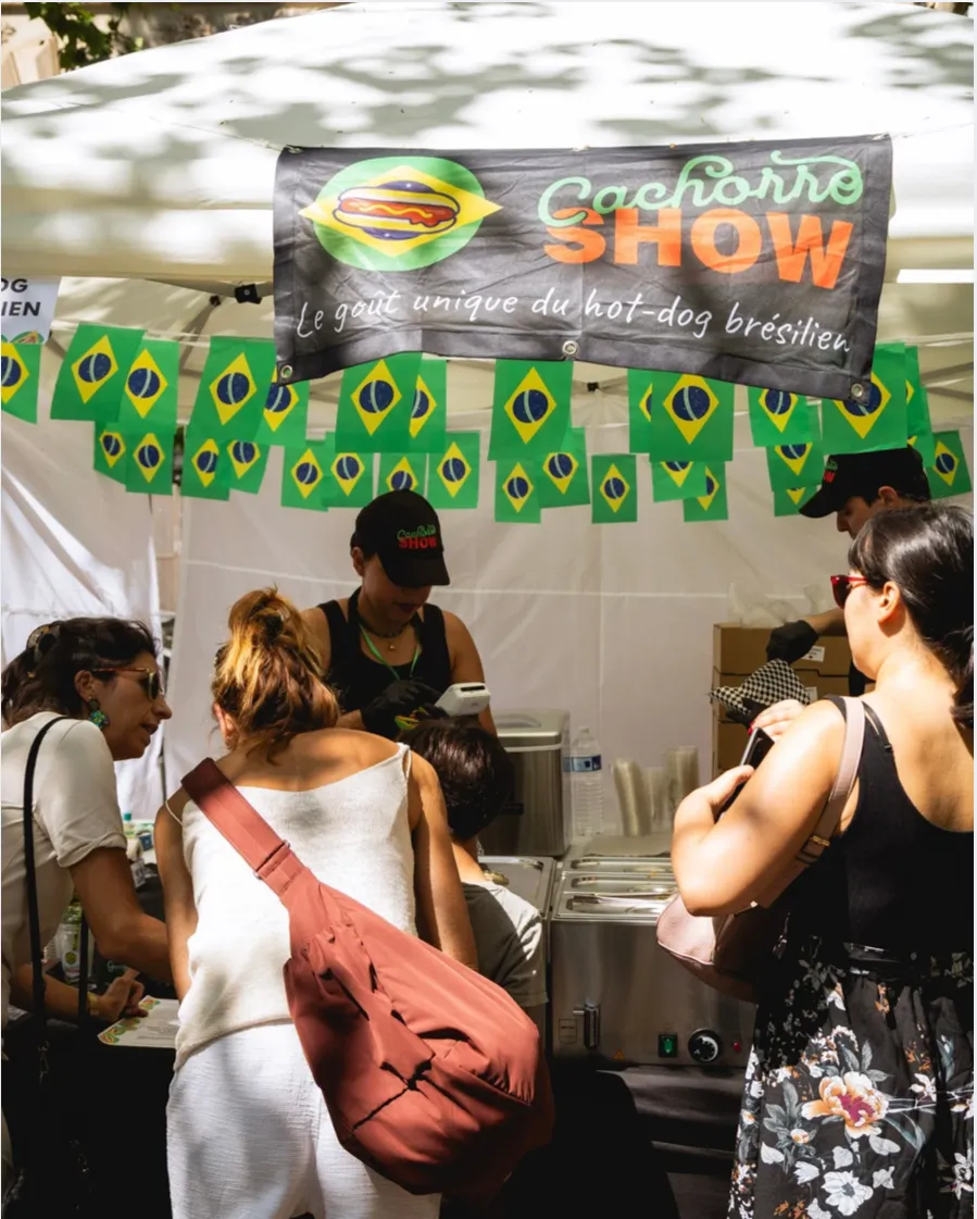 Le stand Cachorro Show sous sa tente, bannière et guirlande de drapeaux brésiliens, clients en file